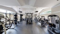 Located at Banyan Grove Lane in Virginia Beach, VA, this fitness center offers a comprehensive workout facility designed to support a wide range of exercise routines. The space is organized into distinct training zones, making it easy to navigate between strength and cardio equipment.

The strength training area is generously outfitted with power racks loaded with weight plates, a multi-functional cable machine system, selectorized strength machines, adjustable benches, and dedicated free weight stations. Mirrors line the walls to assist with form and technique, while the durable rubber flooring throughout provides both safety and comfort underfoot.

The cardio zone features a row of curved treadmills alongside a rowing machine, all positioned in front of large windows dressed with blinds. This area is accented by vibrant chartreuse green walls that add an energizing pop of color, contrasting with the neutral tones found throughout the rest of the facility.

Architecturally, the space boasts vaulted and tray ceilings that amplify the sense of openness, complemented by recessed lighting and ceiling fans that maintain a comfortable environment. Arched windows allow natural light to flood the interior, creating a bright and inviting atmosphere. The overall design balances functionality with an upscale aesthetic, making this fitness center a standout community amenity.
