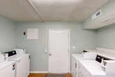 Located at 1011 Gadd Rd in Chattanooga, Tennessee, this shared laundry facility offers a clean, efficiently organized space designed to serve its users with practicality in mind. The room is finished with soft sage-green walls that create a calm, neutral atmosphere, complemented by a textured popcorn ceiling and durable cork flooring underfoot. A centrally positioned door with a glass panel provides access to the facility, allowing for natural visibility and easy entry and exit. Multiple Maytag commercial-grade top-loading washers and dryers are arranged along opposing walls, maximizing the use of available space and accommodating several users simultaneously. The machines are equipped with card and coin payment systems, adding a layer of convenience for residents. A fold-out countertop surface is available for sorting and organizing laundry, and waste bins are provided to keep the room tidy. Overhead fluorescent lighting ensures the space is well-lit throughout. Ventilation is maintained through ceiling vents, and posted informational signage guides users on machine operation and service contacts. The layout is straightforward and user-friendly, making this laundry room a practical and well-maintained amenity for the surrounding residential community.
