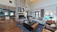 Located at 7428 Muth Ln in Citrus Heights, California, this single-story clubhouse-style space is thoughtfully designed to balance comfort and functionality. The main lounge area serves as the centerpiece of the space, highlighted by a soaring ceiling and a striking floor-to-ceiling river rock fireplace that commands immediate attention. A bold starburst chandelier overhead adds a stylish focal point, while rich hardwood flooring runs throughout, tying the space together. Comfortable seating arrangements, anchored by a patterned area rug, create an inviting gathering environment. Large windows and glass doors along the perimeter flood the interior with natural light and offer direct views of an outdoor pool area, enhancing the connection between indoor and outdoor spaces. A partial river rock accent wall further reinforces the cohesive natural stone aesthetic in the adjacent seating nook. The fully equipped kitchen features vibrant teal walls, white shaker-style cabinetry, dark countertops, stainless steel appliances, open wood shelving, and ample prep space arranged in an efficient L-shaped layout. Abstract artwork throughout adds a contemporary artistic character to the overall ambiance.