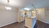 Located at Lake Pointe Village in Orlando, Florida, this single-floor residence offers a well-organized layout with a comfortable, functional design throughout. The open-concept kitchen serves as the heart of the home, featuring light wood cabinetry, white appliances including a side-by-side refrigerator with ice and water dispenser, an electric range, and a dishwasher. A peninsula breakfast bar with pendant lighting extends into the living area, creating a natural divide between the kitchen and the main living space. The living and dining areas are finished with durable hardwood-style flooring and neutral-toned walls, contributing to a bright and cohesive atmosphere. Two bathrooms are present in the unit — each appointed with warm wood vanity cabinetry, light countertops, large mirrors, and hardwood-style flooring. One bathroom includes a shower/tub combination. The bedrooms are generously proportioned, featuring plush wall-to-wall carpeting and windows with blinds that allow natural light to filter in while offering views of the surrounding greenery. The overall palette throughout the residence is neutral and understated, providing a clean canvas that suits a variety of interior styles.