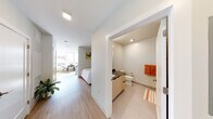 This thoughtfully designed single-floor unit offers a cohesive blend of modern aesthetics and functional living. The open-concept layout connects the living area and kitchen seamlessly, maximizing the sense of space. The living area is anchored by a tufted blue sofa, a round wood coffee table, and a patterned area rug, complemented by vibrant abstract artwork that adds a pop of color to the crisp white walls. Light wood-tone flooring runs throughout, lending warmth and continuity across the space.

The compact kitchen is efficiently outfitted with light wood cabinetry, dark countertops, a stainless steel refrigerator, dishwasher, and a deep single-basin sink. White subway tile backsplash and open shelving add a clean, modern touch to the culinary space.

The sleeping area is positioned adjacent to a large window, allowing natural light to flow in and offering views of the outdoors. A full-size bed dressed in white linens sits beneath a colorful piece of wall art, creating a calm and restful atmosphere.

The bathroom features large-format tile flooring, a vanity with dark countertops and light wood cabinetry, and a clean, minimalist design. Recessed lighting throughout the unit ensures consistent, bright illumination in every room, completing the modern and functional character of this well-planned space.