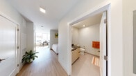 This thoughtfully designed single-floor unit offers a cohesive blend of modern aesthetics and functional living. The open-concept layout connects the living area and kitchen seamlessly, maximizing the sense of space. The living area is anchored by a tufted blue sofa, a round wood coffee table, and a patterned area rug, complemented by vibrant abstract artwork that adds a pop of color to the crisp white walls. Light wood-tone flooring runs throughout, lending warmth and continuity across the space.

The compact kitchen is efficiently outfitted with light wood cabinetry, dark countertops, a stainless steel refrigerator, dishwasher, and a deep single-basin sink. White subway tile backsplash and open shelving add a clean, modern touch to the culinary space.

The sleeping area is positioned adjacent to a large window, allowing natural light to flow in and offering views of the outdoors. A full-size bed dressed in white linens sits beneath a colorful piece of wall art, creating a calm and restful atmosphere.

The bathroom features large-format tile flooring, a vanity with dark countertops and light wood cabinetry, and a clean, minimalist design. Recessed lighting throughout the unit ensures consistent, bright illumination in every room, completing the modern and functional character of this well-planned space.