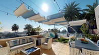 This expansive rooftop terrace offers a well-designed outdoor living experience, combining comfort and style beneath an open Southern California sky. The space is anchored by a central lounge area furnished with white wicker sofas and chairs arranged around a sleek fire pit coffee table adorned with blue glass accents, creating an inviting focal point for gatherings. Overhead, a series of retractable white sail canopies provide adjustable shade, while strands of globe string lights add ambiance for evening use.

To one side, a patch of artificial turf hosts a pair of transparent bubble hanging chairs and a hammock suspended from freestanding frames, offering relaxed, playful seating options with panoramic views of the surrounding palm tree-lined skyline. The terrace floor is finished in warm beige tile throughout, maintaining a cohesive, clean aesthetic.

A dedicated outdoor dining area features a dark table surrounded by matching white wicker chairs, positioned near a full-sized stainless steel gas grill, making the space well-equipped for entertaining. Potted trees and planters are integrated throughout, adding greenery and a resort-like atmosphere. An interior room is accessible directly from the terrace, providing convenient indoor-outdoor connectivity.