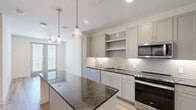 Located in Lewisville, TX, this thoughtfully designed one-bedroom, one-bathroom residence offers a well-appointed single-floor layout that maximizes both functionality and style. The entrance leads into an open-concept kitchen and living area anchored by light wood-look flooring and a clean, neutral color palette. The kitchen is a standout feature, showcasing dark granite countertops on a center island, soft gray shaker-style cabinetry with gold hardware, a subway tile backsplash, and a full suite of stainless steel appliances including a refrigerator, range, microwave, and dishwasher. Elegant pendant lighting with brass accents adds a refined touch above the island. The living area is bathed in natural light, courtesy of a glass-panel door that opens to an outdoor area, complemented by a ceiling fan overhead. The bedroom offers plush carpeting, a ceiling fan, and a window with exterior views, creating a comfortable and restful retreat. A dedicated closet provides organized storage. The bathroom features a granite-topped vanity with gold fixtures, a gold-framed mirror, wood-look tile flooring, and a soaking tub with marble-tiled surround, combining practicality with upscale finishes throughout.