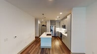Located at 401–451 Crawford St in Fort Worth, Texas, this single-floor residence offers a thoughtfully designed modern interior with a clean, contemporary aesthetic throughout. The open-concept kitchen serves as the centerpiece of the living area, showcasing gray flat-front cabinetry, white quartz countertops, a classic subway tile backsplash, and a full suite of stainless steel appliances including a French door refrigerator, range, and built-in microwave. A large kitchen island with an undermount sink and pendant lighting adds both functionality and style. A built-in wine rack adds a distinctive, practical touch above the cabinetry. Rich hardwood-style flooring runs throughout the main living areas, complementing the bright white walls and recessed lighting to create a warm, inviting ambiance. The living area features a ceiling fan and access to the outdoors through elegant double French doors that flood the space with natural light. The bedroom is finished with plush carpeting, a ceiling fan, and a window with natural views. The bathroom is well-appointed with large-format tile flooring, a tub-shower combination with gray tile surround, and a sleek vanity with ample counter space.