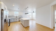 Located at 10650 Sapphire Falls View in Colorado Springs, CO, this single-story home offers five bedrooms and two bathrooms across a well-designed floor plan. The open-concept kitchen and living area serves as the heart of the home, featuring crisp white shaker cabinetry, a tiled backsplash, stainless steel appliances including a French door refrigerator, a gas range, and a built-in microwave. A central island with a white quartz countertop is illuminated by a trio of stylish black and brass pendant lights, providing both workspace and a natural gathering point. Light wood-tone flooring flows seamlessly throughout the entire home, creating a bright, cohesive aesthetic. The living area extends naturally from the kitchen, fitted with a ceiling fan and windows that bring in natural light. Each of the five bedrooms is well-proportioned, with large windows dressed in white blinds offering neighborhood views, and ceiling fans for year-round comfort. The primary bedroom connects to a private bathroom featuring a white vanity with quartz countertop, a lighted mirror, floor-to-ceiling tile surround, a glass-enclosed shower, and direct access to a dedicated walk-in closet with built-in shelving. A second full bathroom serves the remaining bedrooms. Four hallways connect the rooms efficiently throughout the layout.
