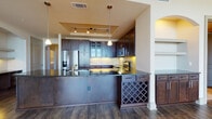 This single-floor high-rise residence is defined by its dramatic floor-to-ceiling glass walls, which frame expansive panoramic views of the city skyline and river below, flooding the living areas with abundant natural light. Rich hardwood flooring runs throughout the open living and dining spaces, complementing the warm, contemporary design aesthetic.

The kitchen is a standout feature, outfitted with dark espresso cabinetry, granite countertops, a tile backsplash, and stainless steel appliances including a double oven and built-in microwave. Pendant lighting illuminates the peninsula, which incorporates a built-in wine rack — an elegant and practical detail. A separate built-in shelving nook with arched detailing adds architectural character nearby.

The bedrooms are carpeted for comfort, with one featuring floor-to-ceiling windows that showcase sweeping views. Both feature walk-in closets with wire shelving systems. The primary bathroom includes a glass-enclosed walk-in shower with tile surround, dark wood vanity cabinetry, and marble-style tile flooring, with direct access to the walk-in closet. A secondary bathroom mirrors the refined finishes with similar cabinetry and tile flooring. An in-unit laundry area with a full-size washer and dryer completes this well-appointed residence.