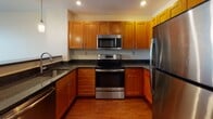 Located at 55 Station in Medford, Massachusetts, this single-floor residence offers a thoughtfully designed layout with a clean, modern aesthetic. Rich hardwood flooring flows consistently throughout the living areas and bedroom, creating a warm and cohesive feel across the space.

The open-concept living area is bathed in natural light from large, floor-to-ceiling windows that offer views of the surrounding Medford neighborhood. The seamless transition into the kitchen makes the space feel expansive and ideal for both everyday living and entertaining.

The kitchen is well-equipped and features warm-toned wood cabinetry, dark granite countertops, and a full suite of stainless steel appliances, including a refrigerator, electric range, and over-the-range microwave. A breakfast bar provides additional counter space and casual seating.

The bedroom is generously sized with a large closet offering built-in hanging storage, and a connecting hallway leads to additional rooms. Neutral, light cream walls throughout the residence complement the hardwood floors and create a bright, airy ambiance.

The bathroom is clean and functional, featuring a full tub-shower combination with chrome fixtures, a wood vanity with dark countertop, and classic white mosaic tile flooring. Together, these spaces combine comfort, practicality, and modern finishes in a convenient Medford location.