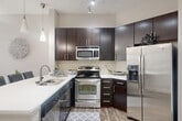 This thoughtfully designed one-bedroom, one-bathroom unit offers an efficient and comfortable layout spread across a single floor. The open-concept kitchen and living area serves as the heart of the home, where rich dark cabinetry, stainless steel appliances, a subway tile backsplash, and light quartz countertops create a sleek, modern kitchen. A breakfast bar with seating connects the kitchen to the living space, making it ideal for casual dining and entertaining. The living room is bright and airy, bathed in natural light from a large sliding glass door that opens onto a private balcony, offering outdoor views and a ceiling fan overhead to enhance comfort. Wood-look flooring flows consistently throughout the unit, tying the spaces together with a warm, contemporary feel. The spacious bedroom accommodates generous furnishings and connects to a dedicated closet with ample storage. The bathroom features a soaking tub with tiled surround, providing a relaxing retreat. Additional conveniences include a dedicated laundry area and hallway, rounding out the functional floor plan. Neutral gray-toned walls and clean white trim throughout the unit create a bright, inviting ambiance well-suited to a variety of interior styles.