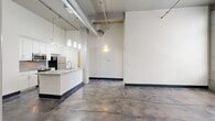 Located at 311 South 11th Street in Richmond, VA, this 2-bedroom, 2-bathroom unit showcases a compelling industrial-chic aesthetic rooted in its converted building origins. Soaring ceilings with exposed metal ductwork and structural beams set a dramatic tone throughout the open-concept living area, while polished concrete floors add a sleek, raw character that flows seamlessly from room to room.

The kitchen is a standout feature, offering white cabinetry, stainless steel appliances, a mosaic tile backsplash, and a generous granite-topped island with a built-in sink — all illuminated by pendant lighting that hangs dramatically from the tall ceiling above. The living area benefits from oversized, industrial-style grid windows that flood the space with natural light and frame views of the surrounding Richmond cityscape.

Both bedrooms continue the concrete floor aesthetic and are served by their own well-appointed bathrooms. Each bathroom features dark tile flooring, granite-topped vanities, white subway tile accents, and modern fixtures, creating a clean, contemporary contrast to the unit's raw industrial elements. Closet space and hallways provide practical storage and connectivity throughout. The overall ambiance is bold yet refined, blending urban character with modern finishes in the heart of Richmond.