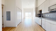 This single-floor unit showcases a clean, contemporary design defined by soaring ceilings and light wood flooring that runs throughout. The open-concept layout connects the kitchen and living area seamlessly, creating a spacious, airy atmosphere filled with natural light.

The kitchen is well-appointed with flat-front white cabinetry extending to ceiling height, dark geometric tile backsplash, dark countertops, and stainless steel appliances including a refrigerator, dishwasher, and built-in microwave. Recessed lighting and a modern faucet complete the functional workspace.

The living area benefits from a large sliding glass door that opens to a balcony, offering outdoor views and allowing abundant natural light to flood the interior. The bedroom is generously sized with tall ceilings, a large window with city views, and direct access to a walk-in closet fitted with wire shelving systems. Additional open shelving is also available near the entry hallway.

The bathroom features light wood flooring, a glass-enclosed shower, a white vanity with dark countertop, a large mirror, and a doorway leading directly to the walk-in closet. In-unit stacked laundry is also present, adding everyday convenience to this thoughtfully designed space.