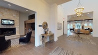 This single-floor clubhouse is thoughtfully designed to offer residents a welcoming and sophisticated communal environment. The space is characterized by soaring ceilings, large arched windows that flood the interiors with natural light, and wide-format tile flooring that flows seamlessly throughout.

Upon entry, a grand hallway connects the various areas of the clubhouse, anchored by a decorative console table and circular mirror that set an elegant tone. To one side, the Java Room features built-in light wood cabinetry, a dark stone tile backsplash, under-counter refrigeration, and a generous countertop — ideal for a self-serve coffee or beverage station.

The main lounge area is a standout feature, centered around a full-height natural stone fireplace with a wall-mounted television above. Adjacent built-in cabinetry with a marble-topped wet bar and dramatic dark stone tile backsplash adds both function and visual interest, complemented by rich leather seating.

A bright sitting area with tall arched windows showcases curated wall art and cozy leather armchairs, offering a relaxed retreat with views of the surrounding landscape. Further into the space, a billiards table and additional seating areas invite social engagement. The overall ambiance balances upscale design with a warm, inviting atmosphere suited for community connection.