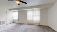 This single-floor unit is thoughtfully laid out to maximize functionality across its key living spaces. The main living area is generously proportioned, featuring plush wall-to-wall carpeting, crisp white walls, and a ceiling fan with integrated lighting. Multiple windows dressed with vertical blinds allow natural light to filter throughout, creating a bright and airy atmosphere. An additional carpeted room serves as a private bedroom, also equipped with a ceiling fan and vertical-blind-covered windows that provide ample daylight and privacy.

The kitchen is well-appointed with rich dark espresso cabinetry, granite countertops, a tile backsplash, and stainless steel appliances including a gas range. An undermount sink with a modern faucet and under-cabinet lighting add practical and aesthetic value. Light-toned tile flooring ties the space together cleanly.

The bathroom features a cohesive design with large-format dark tile extending across the walls and surrounding the soaking tub and shower combination. Light marble-style tile covers the floor, while white cabinetry with brushed nickel hardware beneath a neutral countertop completes the look. Overall, the unit maintains a clean, neutral palette suited to a variety of furnishing styles.