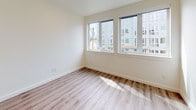 This contemporary apartment showcases a thoughtful design that maximizes space and light. The open-concept living area is anchored by warm, wood-look flooring that extends throughout the unit, creating a seamless flow. Large windows in the main living space and bedroom flood the rooms with natural light, offering views of the surrounding urban landscape.

The kitchen is a highlight, featuring a sleek design with two-tone cabinetry - white upper cabinets and darker lower ones. It's equipped with stainless steel appliances, including a built-in microwave and oven. A distinctive hexagonal tile backsplash adds visual interest, while the countertops appear to be a light-colored quartz or similar material.

The bedroom is generously sized, with ample wall space for furniture placement. A modern ceiling fan ensures good air circulation. The bathroom, while compact, is efficiently designed with a single vanity, toilet, and necessary fixtures. All rooms maintain a neutral color palette, primarily in whites and light grays, which contributes to the bright, airy feel of the space.

The apartment's layout, as seen in the 3D floor plan, shows a logical flow between spaces, with the kitchen, living area, bedroom, and bathroom all easily accessible. This design is ideal for modern, urban living, offering both style and functionality in a compact footprint.