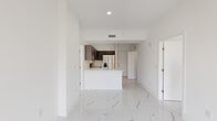 Located at 6–12 Canal St in Miami Springs, FL, this contemporary unit offers a clean, modern aesthetic defined by large-format polished marble-look porcelain tile flooring that flows seamlessly throughout every room, reflecting natural light and creating a bright, airy atmosphere.

The open-concept living and dining area connects directly to a well-appointed kitchen featuring dark wood cabinetry, a quartz waterfall island with an undermount sink, and a full suite of stainless steel appliances including a French door refrigerator, electric range, built-in microwave, and dishwasher. A sliding glass door at the end of the living space opens to a balcony, framing views of swaying palm trees and the surrounding Miami Springs streetscape.

The bedrooms are bright and generously proportioned, with floor-to-ceiling windows that flood the spaces with natural light and offer outdoor views. Both bathrooms continue the marble-look tile theme, with one featuring a soaking tub and tiled surround, and the other showcasing a sleek vanity with quartz countertop, undermount sink, and a separate water closet. Recessed lighting, crisp white walls, and a neutral palette throughout lend the unit a polished, move-in-ready feel well-suited to South Florida living.