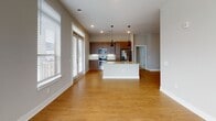 Located at 4429 NC-55 E in Cary, NC, this single-floor unit offers a well-designed, modern layout with a clean, neutral color palette throughout. The open-concept living and kitchen area serves as the centerpiece of the space, featuring warm hardwood-style flooring, large windows with horizontal blinds that invite abundant natural light, and a ceiling fan overhead. The kitchen is equipped with stainless steel appliances — including a refrigerator with ice maker, electric range, and built-in microwave — complemented by rich medium-toned wood cabinetry, granite countertops, and a central island with pendant lighting above. A wide hallway connects the living areas to the private rooms, which are carpeted and include windows with exterior views and ceiling fans. The space includes two bathrooms: one featuring a tub-shower combo with white subway tile surround and brushed nickel fixtures, and another with a glass-door standing shower and matching hardware. Recessed lighting is present throughout, adding to the bright, contemporary ambiance. Crisp white trim and soft gray walls create a cohesive, move-in ready aesthetic across all rooms.