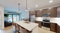 This thoughtfully designed single-floor residence combines modern aesthetics with functional living. The heart of the home is a well-appointed open-concept kitchen featuring rich dark wood cabinetry, white quartz countertops, a full suite of stainless steel Whirlpool appliances, and a white subway tile backsplash. A generously sized center island with an integrated sink and bar seating serves as both a prep area and a casual dining space, illuminated by a pair of stylish pendant lights overhead. Recessed lighting throughout adds to the bright, welcoming atmosphere.

The living area flows seamlessly from the kitchen and is bathed in natural light, thanks to large floor-to-ceiling sliding glass doors that open directly to an outdoor courtyard, blurring the line between indoor and outdoor living. The bedrooms offer plush carpeting, large black-framed windows with courtyard views, and a clean, neutral palette that creates a calm retreat. The bathroom is finished with wood-look flooring, a white quartz vanity, and accessibility-friendly grab bars. A dedicated laundry area rounds out the unit, featuring a stacked Whirlpool washer and dryer alongside matching dark wood cabinetry for additional storage. Light wood-tone flooring ties the main living spaces together cohesively.