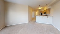 This single-floor residence offers a functional and well-designed layout with a neutral color palette of warm beige tones throughout. The spacious living area is finished with plush carpeting and features multiple windows fitted with blinds, allowing natural light to fill the room. A glass-paneled door leads directly to a private balcony, providing outdoor views of the surrounding neighborhood. A wall-mounted HVAC unit ensures year-round climate control in the living space.

The kitchen is open to the main living area and is anchored by a breakfast bar with granite-style countertops, offering additional seating. Warm-toned wood cabinetry provides generous storage, while stainless steel appliances—including an electric range, over-the-range microwave, and refrigerator—add a modern touch. The kitchen floor features light-toned tile.

The unit includes multiple bedrooms, each carpeted and bright, with windows and ample closet space. One bedroom features a large double-door closet. Two bathrooms serve the unit; both are finished with matching wood vanities, granite-style countertops, and tile flooring. The full bathroom includes a tub-shower combination, while the secondary bathroom offers a single-sink vanity with adjacent toilet.
