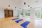 This 720 square foot fitness studio in Fairfax, VA, offers a contemporary and inviting space for exercise and wellness activities. The single-floor layout maximizes functionality with its open concept design. High ceilings create an airy atmosphere, while an array of strategically placed black cylindrical light fixtures provides balanced illumination throughout.

The studio's most striking feature is its abundance of natural light, courtesy of large windows on multiple walls, including clerestory windows that allow sunlight to flood the space. These windows also offer picturesque views of the surrounding greenery, creating a serene backdrop for workouts.

The flooring consists of light-colored hardwood, ideal for various exercise routines and easy maintenance. A wall of floor-to-ceiling mirrors enhances the sense of space and allows for proper form checking during workouts. Built-in wooden shelving units provide ample storage for exercise equipment and personal belongings.

The space is equipped with exercise essentials, including yoga mats, stability balls, and weight training equipment, indicating its versatility for different fitness regimens. Climate control is ensured through visible air conditioning units, maintaining comfort during intense workouts.

This thoughtfully designed studio combines functionality with aesthetic appeal, creating an ideal environment for fitness enthusiasts and wellness practitioners alike.