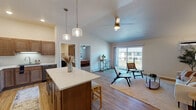 This single-floor residence offers a thoughtfully designed open-concept layout that seamlessly connects the kitchen, dining, and living areas. The kitchen is well-equipped with warm wood cabinetry, stainless steel appliances, a central island with a white countertop and bar seating, and stylish pendant lighting overhead. Light hardwood flooring flows throughout the main living spaces, complementing the bright, neutral color palette.

The living area features vaulted ceilings with a ceiling fan, creating an airy atmosphere. Large sliding glass doors open to a private balcony, filling the space with natural light and providing views of the surrounding exterior. A wall-mounted air conditioning unit ensures year-round comfort.

The bedrooms are carpeted and include ceiling fans and windows with blinds that allow for ample natural light. One bedroom features its own dedicated walk-in closet, complete with built-in shelving, hanging rods, and a central bench — offering generous and well-organized storage.

Both bathrooms are finished with light hardwood-style flooring and dark cabinetry paired with white countertops. One bathroom includes a shower-tub combination, while a second, more spacious bathroom features additional storage cabinetry alongside a tub and shower. The overall design is clean, functional, and consistent throughout the space.