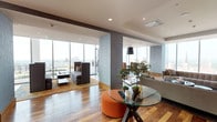The Residences at the Omni Louisville present a masterfully designed high-rise living space that combines contemporary architecture with upscale finishes. Throughout the residence, rich mixed-tone hardwood flooring grounds the interiors, while textured slate-blue accent walls and structural columns add depth and visual interest.

Floor-to-ceiling glass windows dominate nearly every room, flooding the space with natural light and framing sweeping panoramic views of the Louisville skyline. The open-plan living areas are anchored by a media wall featuring custom built-in wood shelving flanking a centrally mounted television, complemented by a pair of tufted grey sofas.

The kitchen is a standout feature, outfitted with warm wood cabinetry, white marble countertops, and a striking row of rose gold globe pendant lights suspended above a long marble-clad island bar. High-end stainless steel appliances complete the culinary space.

Multiple dining configurations serve both intimate and large-scale gatherings, including a round table with leather chairs set against panoramic city views and a generous formal dining table bathed in light from an elegant brass chandelier. Direct access to an outdoor terrace, complete with lounge seating and planted greenery, further extends the living experience.