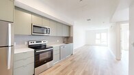 This well-designed single-floor unit offers a thoughtfully arranged layout that maximizes its compact footprint. Light hardwood flooring runs continuously throughout the space, creating a cohesive and airy feel across every room.

The kitchen is a standout feature, showcasing a full suite of stainless steel appliances, including a refrigerator, electric range, over-the-range microwave, and dishwasher. Sage-toned flat-front cabinetry extends from floor to ceiling, providing generous storage, while a textured tile backsplash and clean white countertops add a polished, modern aesthetic. The kitchen flows openly into the living area, enhancing the sense of space.

The bedroom is comfortably sized and filled with natural light from a large window that frames scenic outdoor views, including palm trees and distant hills. A sliding closet with a rod system offers practical built-in storage. The clean white walls and light flooring contribute to the room's bright, calm atmosphere.

The bathroom features a full soaking tub and shower combination with white subway tile surround, complemented by brushed gold fixtures. A vanity with a built-in sink and the same light hardwood flooring complete the clean, minimalist design. Overall, the unit presents a fresh, modern aesthetic throughout.