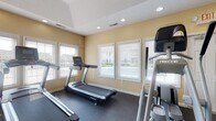 Located at 5222 Flower Valley Dr in Canal Winchester, Ohio, this single-floor fitness center is a well-equipped community exercise facility designed to support a full range of workout routines. The space is bathed in natural light, courtesy of multiple large windows fitted with white horizontal blinds that line the walls, offering views of the surrounding neighborhood while maintaining privacy.

The fitness center is thoughtfully laid out to accommodate both cardio and strength training. The cardio zone features multiple treadmills and elliptical machines, providing ample options for aerobic exercise. A cable and pulley strength system by BodyCraft anchors the strength training area, complemented by floor exercise mats and resistance accessories. Full-length mirrors along one wall enhance the sense of space and allow users to monitor their form during workouts.

The flooring throughout is durable rubber gym matting, ideal for high-traffic exercise use and impact absorption. Recessed lighting in the ceiling provides consistent illumination across the entire space. Amenities include a wall-mounted water fountain, a first aid station, a fire extinguisher, and clearly posted safety and facility guidelines. The room is served by multiple HVAC vents and includes both an entry door and a marked exit door, ensuring proper ventilation and safety compliance.
