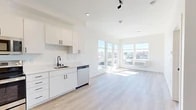 Located on the fourth floor at 2002 N Monroe Street in Spokane, Washington, this contemporary unit offers a thoughtfully designed single-floor layout. The open-concept living and kitchen area is bright and airy, filled with natural light streaming through expansive floor-to-ceiling windows that frame sweeping views of the surrounding Spokane cityscape. Light-toned luxury vinyl plank flooring flows consistently throughout, complementing the clean, white interior palette.

The kitchen is well-appointed with crisp white cabinetry featuring matte black hardware, a stainless steel refrigerator, electric range, built-in microwave, and dishwasher — all set against a seamless white countertop with an undermount sink and sleek black gooseneck faucet. Track lighting overhead adds a modern touch. The open layout transitions naturally into the living area, which benefits from a corner window configuration that maximizes both light and views.

The bedroom is a serene, sun-filled space with a large window overlooking the city and a dedicated walk-in closet outfitted with wire shelving. The bathroom features a clean modern design with a round mirror, white vanity, and warm wood-toned flooring. A dedicated laundry area with a full-size washer and dryer adds everyday convenience to this efficiently designed Spokane residence.