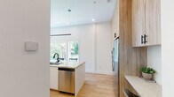 Located at 313 SE Second St in Bentonville, Arkansas, this single-story space showcases a clean, contemporary design characterized by white walls, light hardwood flooring, and warm wood-toned cabinetry throughout. The open-concept kitchen serves as a central highlight, featuring floor-to-ceiling natural wood cabinetry, stainless steel appliances, a subway tile backsplash, and a generously sized island with a stone countertop, undermount sink with a matte black faucet, and seating for multiple guests. A linear pendant light anchors the space, while large windows invite abundant natural light and outdoor views. A dedicated built-in desk area off the kitchen provides a functional workspace. The living area is bright and welcoming, with large glass doors opening directly to an outdoor space overlooking lush greenery. The bedroom continues the refined aesthetic with tall ceilings, hardwood floors, and direct access to the outdoor area through floor-to-ceiling glass doors. The bathroom features a floating wood vanity with matte black fixtures, a round mirror, and a glass-enclosed walk-in shower with large-format tile. An in-unit stacked washer and dryer complete this well-appointed space.