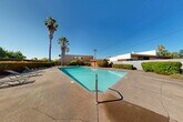 Located at 4730 El Camino Ave in Arden-Arcade, California, this single-level property features a generously sized outdoor swimming pool as its centerpiece. The pool area is surrounded by a wide concrete deck with poolside lounge chairs, offering ample space for relaxation and recreation. Towering palm trees and well-maintained hedges and shrubs frame the perimeter, providing a degree of privacy while enhancing the California outdoor aesthetic.

The adjacent building showcases a distinctive mid-century architectural style, characterized by a sawtooth roofline with angled wood beams and expansive floor-to-ceiling windows that allow abundant natural light to fill the interior. The warm-toned exterior combines wood accents with neutral stucco siding, creating a cohesive and inviting facade that overlooks the pool courtyard.

A small red outbuilding near the pool serves as an accessory structure, likely housing pool equipment or storage. Seating areas with tables and chairs are positioned along the building's exterior, ideal for outdoor gatherings. The landscaping throughout the space includes a variety of shrubs, ornamental plants, and mature trees, contributing to a vibrant and well-kept environment. The site benefits from the region's characteristic abundant sunshine, making this outdoor amenity a standout feature of the property.