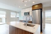 Located at 301 M St SW in Washington, DC, this two-bedroom, three-bathroom residence offers a thoughtfully designed single-floor layout with modern finishes throughout. The open-plan living and dining area flows seamlessly from the kitchen, creating an inviting, connected space filled with natural light from large windows and sliding glass doors. Light wood-tone flooring runs throughout, lending warmth and continuity to every room.

The contemporary kitchen is a standout feature, centered around a curved island with a white quartz countertop, an undermount sink, and a sleek arc faucet. Two-tone cabinetry pairs high-gloss white uppers with rich walnut-finish lowers, complemented by stainless steel appliances including a built-in oven, cooktop, microwave, and full-size refrigerator. A white tile backsplash and recessed track lighting complete the polished aesthetic.

The primary bedroom includes an en-suite bathroom featuring marble-look tile in the glass-enclosed walk-in shower, a floating wood vanity, and tile flooring. An exposed concrete accent column adds an industrial touch. Additional bathrooms mirror the refined design. Four closets, including a walk-in with built-in shelving, offer generous storage. A private patio accessed via sliding doors provides outdoor space with open city views.