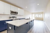 This single-floor, 2-bedroom, 2-bathroom residence in Sparks, Nevada, offers a clean, contemporary design throughout. The open-concept kitchen serves as the centerpiece of the main living area, showcasing a striking two-tone cabinet scheme with crisp white upper cabinets and bold navy blue lower cabinets and island base. Light quartz countertops, a white subway tile backsplash, stainless steel appliances—including a refrigerator, range, and over-the-range microwave—and an island with seating overhang complete the well-appointed kitchen. An in-unit stacked washer and dryer is conveniently accessible just off the kitchen. The open living area extends from the kitchen toward a wide window that draws in natural light and provides views of the surrounding neighborhood. Light-toned wood-look flooring runs throughout the main living spaces, contributing to a bright, cohesive aesthetic. Both bedrooms are comfortably sized, featuring neutral carpet flooring and large windows that allow ample natural light. Each bathroom is finished with white cabinetry, quartz countertops, a large vanity mirror, and a tub-shower combination, maintaining the home's consistent, modern style.