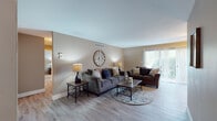 This single-floor residence offers a thoughtfully designed layout that balances comfort and functionality across its key living spaces. The living room serves as the heart of the home, featuring warm, neutral-toned walls, light wood-style flooring, and a large sliding glass door fitted with vertical blinds that invites natural light and provides access to the outdoors. The open seating arrangement is anchored by a decorative round wall clock, creating a welcoming and cohesive atmosphere.

Adjacent to the living area, the dining space accommodates a full dining set beneath a ceiling fan with lighting, with another sliding glass door offering additional natural light and outdoor access. The galley-style kitchen is efficiently organized with white cabinetry, dark countertops, a stainless steel sink, and appliances including a refrigerator and dishwasher, complemented by track lighting overhead.

The primary bedroom features plush carpeting, a ceiling fan, and neutral walls that create a calm retreat. A second bedroom, also carpeted, offers ample space and a window with sheer curtains, suitable for various uses. The full bathroom is finished with white tile surrounding a tub-shower combination and includes wood-style flooring. Throughout the residence, consistent finishes and a neutral color palette contribute to a clean, cohesive aesthetic.