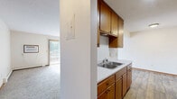Located at 1200 Autumn Dr in Faribault, MN, this 2-bedroom, 1-bathroom unit offers a practical and comfortable single-floor layout. The galley-style kitchen features warm wood cabinetry, white appliances including an electric range and refrigerator, a double-basin sink, and durable wood-look flooring. An adjacent dining area provides a dedicated space for meals. The living room is generously proportioned, filled with natural light streaming through a sliding glass door that opens onto a private balcony with outdoor views — a standout feature of the unit. Carpeted flooring runs throughout the living areas and bedrooms, adding warmth underfoot. The primary bedroom is notably spacious, benefiting from two windows that invite natural light and views of the surrounding greenery, along with an expansive walk-in closet featuring dual hanging rods. The second bedroom is comfortably sized with its own window and closet. The bathroom includes a full tub-shower combo with a white surround and wood-look flooring. With five closets total distributed throughout, storage is plentiful. Baseboard heating is present in the main living areas and bedrooms, ensuring year-round comfort in this well-organized and functional home.