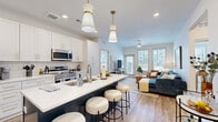 This well-appointed 2-bedroom, 2-bathroom residence is laid out on a single floor, offering a thoughtfully designed open-concept floor plan. The combined kitchen and living area serves as the heart of the home, where a striking navy-blue kitchen island with white quartz countertops and seating for multiple guests anchors the space. The kitchen features white shaker cabinetry with gold hardware, a white subway tile backsplash, and a full suite of stainless steel appliances, all illuminated by stylish pendant lighting. The living area flows seamlessly from the kitchen and is bathed in natural light from large windows and a glass door that provides views of the surrounding cityscape. Both bedrooms are carpeted and generously sized, each benefiting from multiple windows that fill the rooms with natural light. The primary bedroom includes a dedicated closet with built-in wire shelving systems for organized storage. Each of the two bathrooms is finished with white cabinetry accented by gold hardware, white quartz vanity tops, and tiled shower-tub combinations. Wood-look flooring runs throughout the main living areas and bathrooms, lending warmth and continuity to the overall design. A hallway connects the private bedroom wing to the main living spaces, completing this cohesive and functional layout.