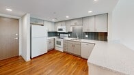 This thoughtfully laid-out one-bedroom, one-bathroom residence offers a clean, modern aesthetic across a single floor. The open-concept living and kitchen area serves as the heart of the home, featuring warm hardwood flooring throughout. The kitchen is well-appointed with gray shaker-style cabinetry, a tiled backsplash in a stacked slate pattern, light stone countertops, a kitchen island for additional prep space, and a full suite of white appliances including a refrigerator, electric range, microwave, and dishwasher. Recessed lighting illuminates the space efficiently.

The living area flows seamlessly from the kitchen and opens directly to a private balcony through a wide sliding glass door framed by dark curtains, allowing abundant natural light and exterior views. The bedroom offers a comfortable footprint, carpeted flooring, and its own access to the balcony via a second sliding door. Two closets provide ample storage throughout the unit.

The bathroom features classic white mosaic tile flooring, a full tub-shower combination, and a vanity with a dark stone countertop and built-in cabinetry. Crisp white walls and clean lines throughout give the entire residence a bright, contemporary feel.