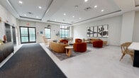 Located at 10 W Westfield Ave in Roselle Park, NJ, this thoughtfully designed lobby and common area serves as a welcoming gateway for residents. The single-floor space is generously proportioned, offering an open, airy atmosphere enhanced by large windows that invite abundant natural light throughout the day. The ceiling features elegant tray detailing with recessed lighting, adding architectural depth and a refined sense of scale.

The lounge area is anchored by a curated selection of contemporary furnishings, including curved velvet sofas in warm caramel and bold rust tones, paired with ribbed accent chairs and natural wood side tables. Layered area rugs define the seating zones, while a series of striking abstract framed artworks adorns the walls, contributing to the space's modern aesthetic.

A dedicated dining area features a long communal table with sleek wooden chairs, lit by a modern globe pendant fixture — ideal for casual gatherings. Adjacent to the lounge, a dramatic black steel-framed glass partition wall and double-door entry creates a sophisticated interior threshold.

The elevator vestibule showcases a textured, patterned accent wall with elegant wall sconces and a decorative console, providing a polished transition point. The light-toned large-format tile flooring flows seamlessly throughout, unifying each zone into a cohesive and inviting communal environment.