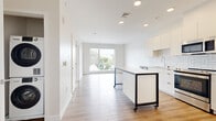 Located at 50 Salt St, Unit 457 in Revere, MA, this thoughtfully designed unit offers a bright, modern living experience across a single floor. The open-concept layout seamlessly connects the kitchen and living areas, creating an efficient and functional flow throughout the space. Light wood-tone flooring runs continuously throughout, complementing the crisp white walls and recessed lighting overhead.

The contemporary kitchen is a standout feature, outfitted with sleek white cabinetry, a geometric tile backsplash, stainless steel appliances including a dishwasher, range, microwave, and refrigerator, and a white quartz countertop. A mobile kitchen island with a bold black metal frame provides additional prep space and flexibility.

The living areas benefit from generous natural light, with large floor-to-ceiling windows that frame views of the surrounding Revere neighborhood and tree canopy. The bright, airy atmosphere is further enhanced by the neutral color palette throughout.

The bathroom is finished with marble-look tile flooring, a wood-toned vanity with a white countertop, a large mirror, and a full tub and shower combination with clean white tile surround. A hallway with a closet provides practical storage. The unit also includes dedicated closet space, adding to its overall functionality.