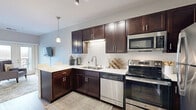 Located at 4143 Centerville Rd in Vadnais Heights, MN, this one-bedroom, one-bathroom unit offers a thoughtfully designed single-floor layout that maximizes every square foot. Rich hardwood-style flooring flows throughout, complementing a neutral color palette that creates a clean, modern aesthetic.

The kitchen is a standout feature, showcasing rich dark espresso cabinetry paired with crisp white quartz countertops and a classic white subway tile backsplash. A full suite of stainless steel appliances — including a refrigerator, electric range, microwave, and dishwasher — lines the walls, while a peninsula with bar seating and pendant lighting above adds both functionality and style. Track lighting further enhances the kitchen's modern character.

The spacious primary bedroom offers a serene retreat, featuring natural light from a set of glass doors that open directly onto a private balcony with outdoor views. The room comfortably accommodates a full bedroom set and includes a wall-mounted television area.

The bathroom is well-appointed with dark espresso cabinetry, a white quartz vanity top, a large mirror, and a full shower with a tub. Wood-look flooring extends here as well, maintaining design continuity throughout.

A dedicated in-unit laundry closet houses a full-sized top-load washer and dryer with built-in shelving above, providing added convenience.