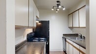 This single-floor residence offers a thoughtfully arranged layout that balances functionality and comfort throughout. The open living area serves as the heart of the home, featuring rich, dark hardwood-style flooring, a ceiling fan, and a sliding glass door that floods the space with natural light and provides views of the outdoors. A breakfast bar connects the living area to the galley-style kitchen, which is equipped with dark granite-style countertops, white cabinetry with warm wood trim, black appliances including an electric range and refrigerator, a dishwasher, and a stainless steel sink. Track lighting overhead enhances the kitchen's functionality. A hallway with wood-toned doors leads from the main living space to the private areas of the residence. The bedrooms are finished with plush carpeting and feature windows with blinds that allow for natural light, while built-in closets with wood-framed doors and hanging rods provide ample storage. The bathroom includes a soaking tub, a toilet, a vanity with matching countertops, and stone-look tile flooring that adds a grounded, earthy aesthetic. Throughout the residence, neutral wall tones and consistent finishes create a cohesive and inviting atmosphere.
