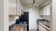 This single-floor residence offers a thoughtfully arranged layout that balances functionality and comfort throughout. The open living area serves as the heart of the home, featuring rich, dark hardwood-style flooring, a ceiling fan, and a sliding glass door that floods the space with natural light and provides views of the outdoors. A breakfast bar connects the living area to the galley-style kitchen, which is equipped with dark granite-style countertops, white cabinetry with warm wood trim, black appliances including an electric range and refrigerator, a dishwasher, and a stainless steel sink. Track lighting overhead enhances the kitchen's functionality. A hallway with wood-toned doors leads from the main living space to the private areas of the residence. The bedrooms are finished with plush carpeting and feature windows with blinds that allow for natural light, while built-in closets with wood-framed doors and hanging rods provide ample storage. The bathroom includes a soaking tub, a toilet, a vanity with matching countertops, and stone-look tile flooring that adds a grounded, earthy aesthetic. Throughout the residence, neutral wall tones and consistent finishes create a cohesive and inviting atmosphere.