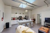 Located at 77 Main St in Cortland, NY, this three-bedroom, one-bathroom unit offers a thoughtfully designed single-floor layout with notable industrial-modern character. The open-concept living and kitchen area is the heart of the home, distinguished by soaring ceilings, exposed ductwork, and a large overhead skylight that floods the space with natural light. A geometric pendant light fixture adds a contemporary accent above the central kitchen island, which features a granite countertop and bar seating. The kitchen is well-appointed with white shaker cabinetry, granite countertops, and a full suite of stainless steel appliances including a refrigerator, electric range, and microwave. The living area flows seamlessly from the kitchen, creating an open and functional shared space. Wide-plank hardwood-style flooring extends throughout the main living areas and bedrooms, lending warmth and cohesion. The primary bedroom is generously proportioned with tall ceilings, while the additional bedrooms offer natural light through large windows with sheer curtains. The bathroom features a clean, light palette with a white vanity, framed mirror, and a shower/tub combination.