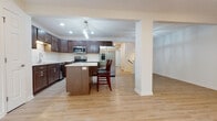 This two-story home is designed with a cohesive, contemporary aesthetic that carries throughout both levels. The main floor is anchored by a generous living area finished with warm hardwood-style flooring, recessed lighting, and a ceiling fan. Large windows and a sliding glass door flood the space with natural light while offering views of surrounding greenery, creating a bright and inviting atmosphere. A fireplace adds a functional focal point to the living area.

The kitchen is well-appointed with rich cherry-toned cabinetry, white countertops, and a full suite of stainless steel appliances, including a refrigerator with ice maker, range, microwave, and dishwasher. A central island with seating provides additional prep space and a casual dining option. Pendant and track lighting enhances the kitchen's functionality and visual appeal.

The main floor also features a wide hallway leading to carpeted stair access to the upper level. Upstairs, bedrooms are finished with plush carpet and ceiling fans, benefiting from ample natural light through multiple windows. Bathrooms on both levels include warm wood-toned vanities, and feature either a walk-in shower or a tub-shower combination. A dedicated laundry area houses a full-size front-loading washer and dryer with overhead shelving for storage.
