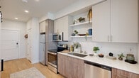 This thoughtfully designed one-bedroom, one-bathroom unit makes efficient use of its compact footprint, offering a modern and cohesive aesthetic throughout. Light hardwood flooring runs continuously across all rooms, lending a warm, unified feel to the space.

The galley-style kitchen is a standout feature, showcasing two-tone cabinetry with warm wood-grain lower cabinets and white upper cabinets, complemented by white quartz countertops and a subway tile backsplash. A full suite of stainless steel appliances — including a refrigerator, electric range, built-in microwave, and dishwasher — provides everyday functionality, while open shelving adds both storage and a stylish display area.

The living room benefits from multiple windows fitted with white horizontal blinds, allowing an abundance of natural light to fill the room. The bright, neutral walls create a versatile backdrop for a variety of furnishing styles.

The bedroom is a calm and comfortable retreat, featuring a sliding closet door, a window for natural light, and clean white walls that enhance the sense of openness.

The bathroom continues the modern design language with a wood-tone vanity, white quartz countertop, a large wall mirror, and a shower-tub combination. Recessed lighting and a crisp white palette complete the polished, contemporary look throughout this well-appointed unit.