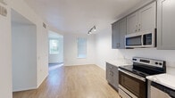 Located on iconic Sunset Boulevard in Los Angeles, this 1-bedroom, 2-bathroom residence offers a well-designed, efficiently laid-out living space on a single floor. The open-concept kitchen and dining area serves as the heart of the home, showcasing gray shaker-style cabinetry, marble-veined quartz countertops, and a full suite of stainless steel appliances including a range, microwave, dishwasher, and refrigerator. Light hardwood-style flooring runs throughout, complementing the crisp white walls and creating a bright, cohesive aesthetic. Track lighting and natural light from multiple windows enhance the airy feel of the living and dining area. The bedroom is a comfortable retreat featuring a mirrored sliding closet and a window that allows natural light to fill the room. Both bathrooms are finished with gray vanities topped with quartz counters, large mirrors, and white tiled tub-shower combinations, maintaining a clean and modern look. A dedicated closet provides additional storage. The building itself features a landscaped courtyard with lush greenery and open-air walkways, adding a welcoming communal element to this centrally located Hollywood residence.