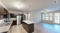 Located at 606 SW 29th Ave in Cape Coral, Florida, this two-story home offers 2 bedrooms and 2 bathrooms across a well-organized layout. The main living level hosts the majority of the space, while the ground floor provides an attached garage with a concrete floor and automatic opener. A staircase connects both levels, leading up to the bright, open-concept kitchen and living area. The kitchen is outfitted with dark espresso cabinetry, granite-style countertops, stainless steel appliances including a refrigerator, range, microwave, and dishwasher, and a central island with pendant lighting above. Light wood-style flooring extends throughout the main living area, which benefits from a ceiling fan and windows that invite natural light. The primary bedroom is generously sized, featuring a ceiling fan, large windows with exterior views, and access to a dedicated closet. The second bedroom offers plush carpeting, a ceiling fan, and its own closet. Both bathrooms are finished with dark vanities, granite-style countertops, and tub-shower combinations with clean white surrounds. A dedicated in-unit laundry room accommodates a full-size washer and dryer. The overall aesthetic is modern and cohesive throughout.