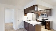 This single-floor residence offers a thoughtfully designed layout encompassing a welcoming entrance, an open-concept living and kitchen area, one generously sized bedroom, and a dedicated laundry room. The living room is bright and open, featuring plush wall-to-wall carpeting, neutral white walls, and a sliding glass door that fills the space with natural light and provides direct access to a private outdoor area. The kitchen is a functional centerpiece of the home, featuring rich dark-espresso cabinetry, a peninsula with a white countertop and built-in sink, and a full suite of stainless steel appliances including a refrigerator, electric range, and microwave. A skylight overhead bathes the kitchen in additional natural light, while tile flooring adds a clean, durable finish. The spacious primary bedroom is carpeted and bright, with a window offering natural light and direct access to a full bathroom. The laundry room includes a stacked washer and dryer unit with wire shelving for added storage convenience. Throughout the residence, the clean white walls, consistent flooring choices, and practical layout create a cohesive and comfortable living environment.