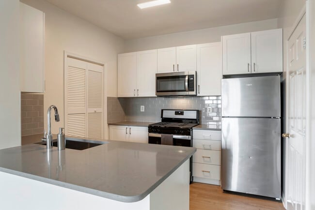 Renovated Package II kitchen with white cabinetry, grey quartz countertops, tile backsplash, stainless steel appliances, and hard surface flooring - Avalon Reston Landing