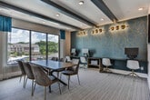 Located in Atlanta, GA, this single-floor business center offers a well-appointed environment tailored for professional meetings and focused work. The centerpiece of the space is a generously sized conference room featuring a long wooden boardroom table surrounded by leather mid-century modern chairs. A large picture window dressed with teal and white curtains floods the room with natural light and provides open views of the surrounding neighborhood. Vibrant, colorful artwork adorns the walls, adding a creative energy to the professional setting. Recessed lighting and a tray ceiling lend a polished, contemporary feel to the room.

Adjacent to the conference room, a dedicated computer workstation area offers multiple desktop computers and a printer along a sleek wall-mounted desk. This zone is distinguished by a striking teal and gold geometric accent wall, illuminated by a row of gold globe sconces that create a warm, stylish ambiance. White modern chairs with gold-toned legs complete the look.

The two areas are connected via floor-to-ceiling black-framed glass sliding doors, maintaining an open sightline while allowing for privacy when needed. A wall-mounted mini-split HVAC unit ensures individual climate control. Neutral-toned carpet tile flooring runs throughout, tying the space together with a clean, professional finish.