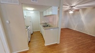This single-floor 1-bedroom, 1-bathroom unit offers a practical and efficiently designed layout. The living area features warm wood-look flooring, a ceiling fan with light fixture, a textured ceiling, and a window fitted with blinds that allows natural light to filter in through the entryway space.

The kitchen is designed as a galley-style corridor, equipped with white cabinetry, a double-basin sink with a granite-look countertop, and white appliances including a refrigerator and electric range. A pass-through window with a countertop bar connects the kitchen directly to the living area, creating an open sightline between the two spaces and enhancing the sense of connectivity throughout the unit.

The bathroom is neatly appointed with a single vanity featuring a speckle-finish countertop, a wall-mounted mirror with an overhead light bar, a toilet, and a tiled shower-tub combination. Wood-look flooring continues into the bathroom, maintaining a cohesive aesthetic throughout the unit.

Textured ceilings are consistent throughout the space, and ample ventilation is provided via ceiling vents. The overall design is clean and functional, with a neutral color palette of soft beige and white tones that creates a bright, understated ambiance suitable for comfortable everyday living.